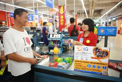 沃尔玛购物广场北京宣武门店收银员正在向顾客介绍你“沃”一起，为爱加餐项目的捐款信息。