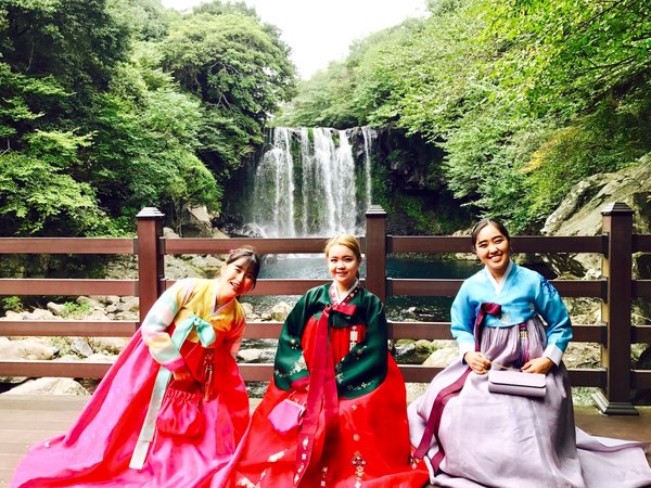 Tourists are enjoying a trip in front of Jeju waterfall, wearing hanbok