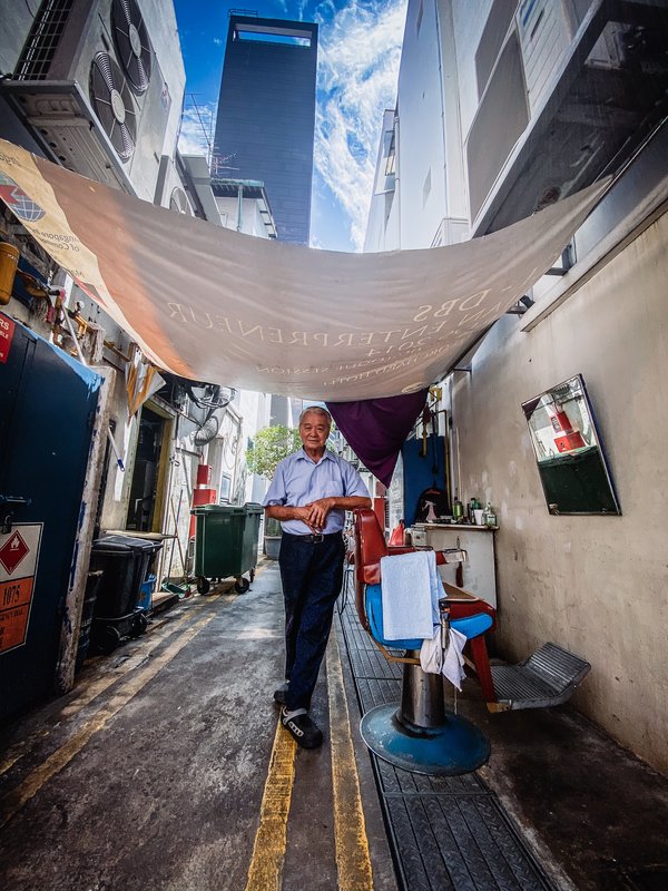 アイク・ベン・チア氏の撮影による、The Clan Hotel Singaporeを背景にしたテロックアヤ通りの路上理髪師