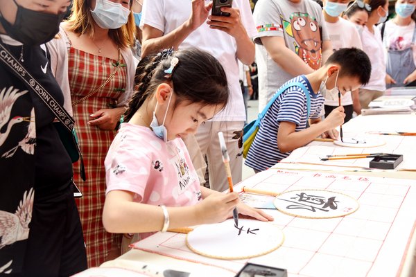 游客们正在使用晨光毛笔在团扇上书写汉字，感受手写的温度
